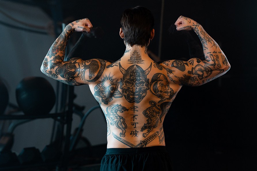 En mand ses fra bagsiden, og han spnder i sine muskler i et fitnesslokale.
